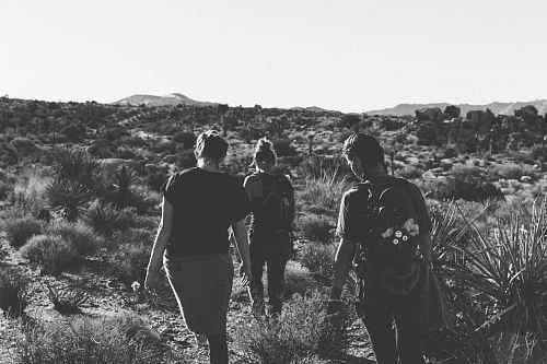 grayscale photography of three women trekking on empty field