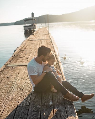 man and girl sitting on brown dock near boat and two white ducks during daytime