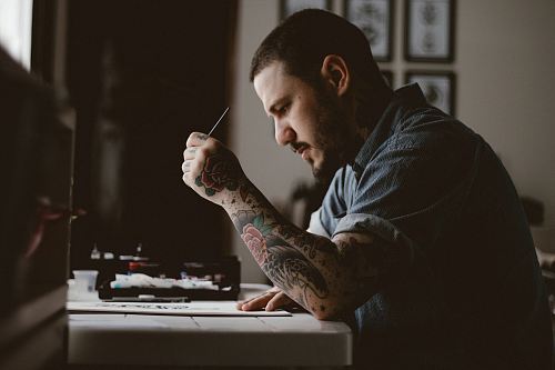 man holding pen and paper sitting near table facing outside in a dim-lit room during daytime