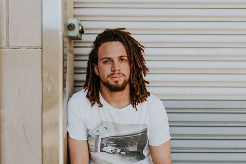 man sitting near gray steel roller shutters during daytime