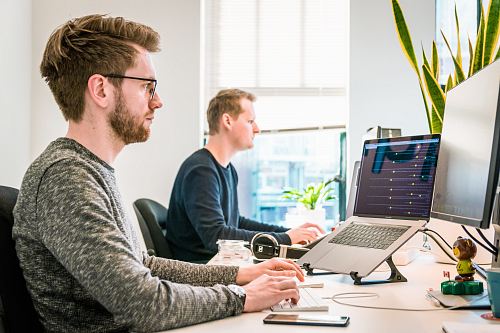 man sitting on chair wearing gray crew-neck long-sleeved shirt using Apple Magic Keyboard