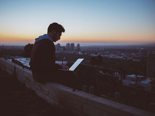 man sitting on concrete brick with opened laptop on his lap