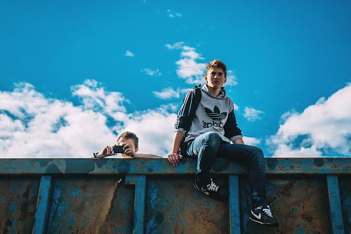 man sitting on rail beside man holding camera