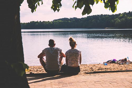 men and woman sitting on pavement facing body of water