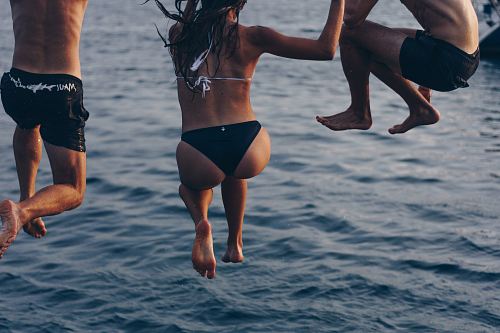 one woman and two men jumping at sea