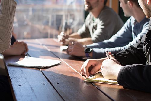 people sitting on chair in front of table while holding pens during daytime