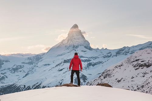person in red hoodie standing on snowy mountain during daytime