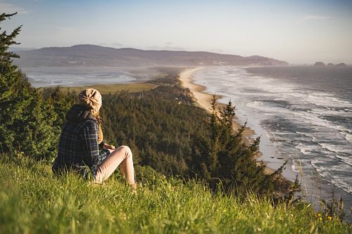 person sitting on hill near ocean during daytime