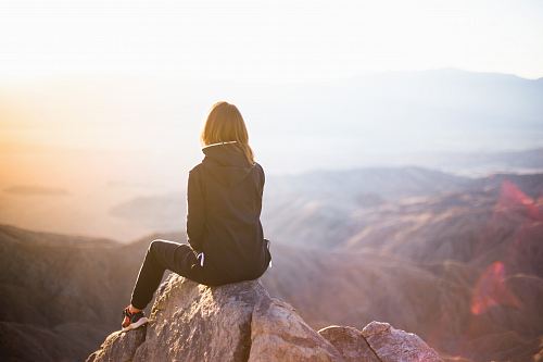 person sitting on top of gray rock overlooking mountain during daytime