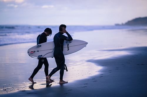 person walking on seashore holding surfboard