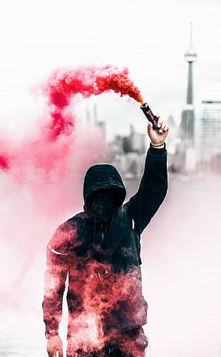 person wearing black and red hoodie holding smoke bomb
