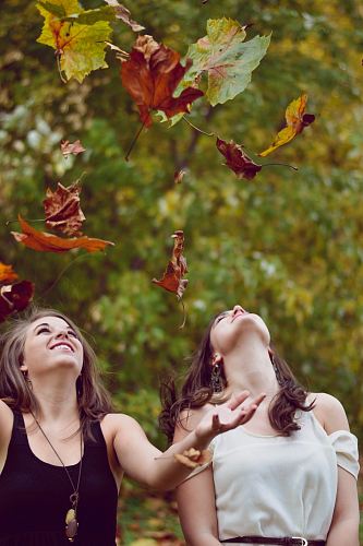 photo of two women throwing leaves during daytime