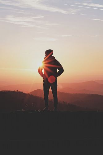 silhouette of man standing near cliff in golden hour background