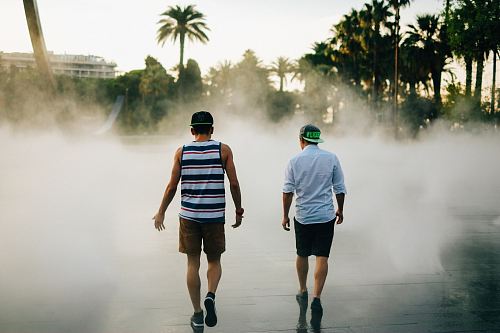 street photography of two men walking in front of water fountain