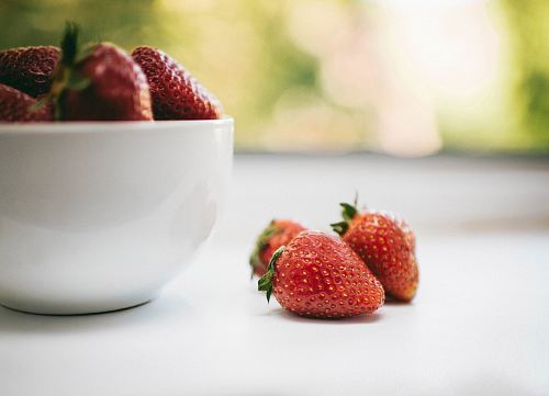 three red strawberries beside bowl with strawberries