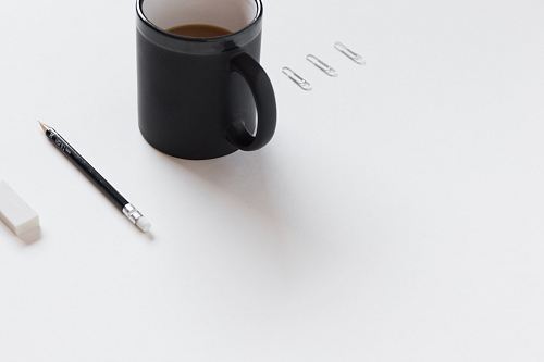 three white paper clips, black ceramic mug, black pencil, and white pencil eraser on white surface