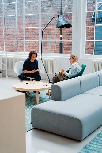two woman sits on sofa chairs inside house