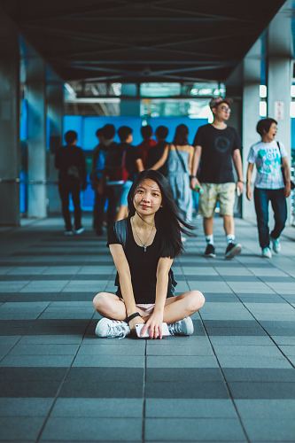 woman carrying backpack while sitting cross legs on hallway in front of people walking