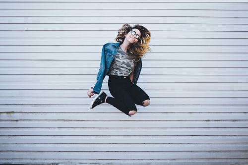 woman jumping in front of white concrete establishment