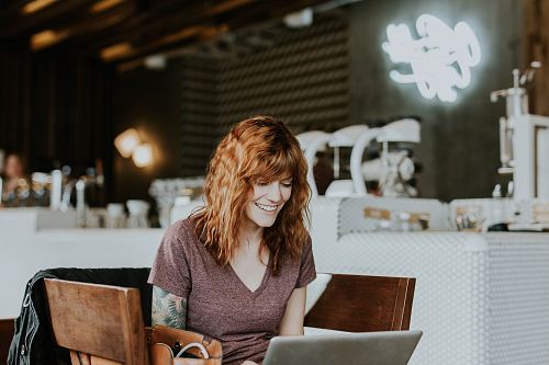 woman sitting on brown wooden chair while using silver laptop computer in room