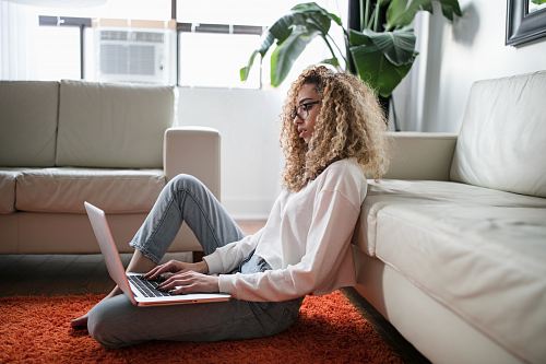 woman sitting on floor and leaning on couch using laptop