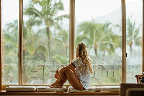 woman sitting on white cushion near glass window