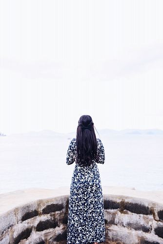 woman wearing black and white long sleeve dress standing facing sea during daytime
