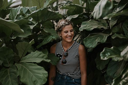 woman wearing black and white striped sleeveless shirt surrounded by green plants smiling posting for photo