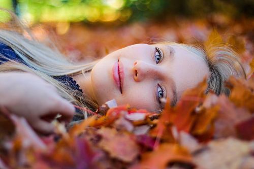 woman wearing blue top lying on dried maple leaves during daytime photography