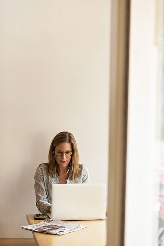 woman wearing grey striped dress shirt sitting down near brown wooden table in front of white laptop computer