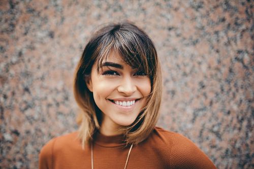 woman with brown hair in brown shirt smiles near brown wall