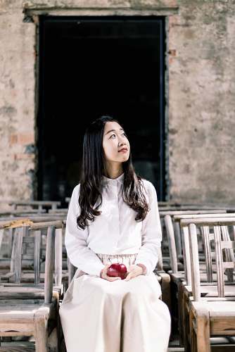 woman woman in white button-up dress shirt and white pants holding apple sitting on chair apple