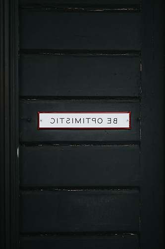 sign black wooden door with be optimistic text overlay words