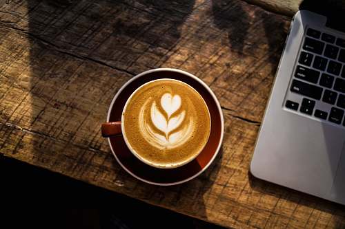 cup caffe latte on white ceramic cup beside silver and black laptop computer drink