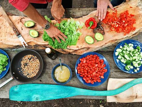 fruit person slicing green vegetable in front of round ceramic plates with assorted sliced vegetables during daytime avocado