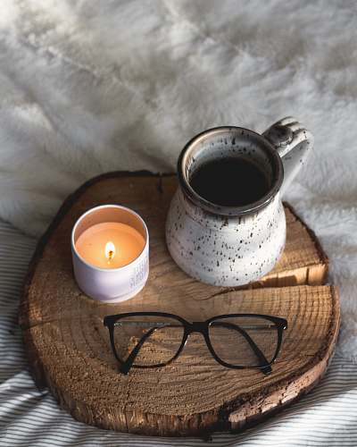 cup black-framed eyeglasses beside candle coffee cup
