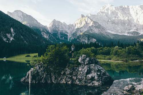  person standing on rock formation surrounded by body of water 