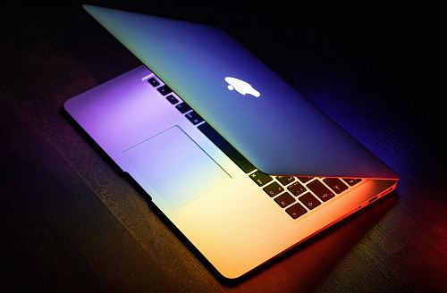 A MacBook lit up in rainbow colors on a wooden surface