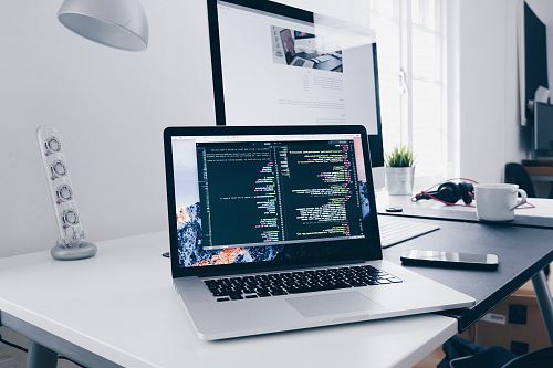 A MacBook with lines of code on its screen on a busy desk