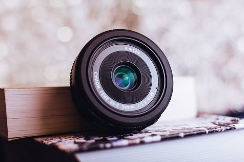 black Canon camera lens leaning on white book