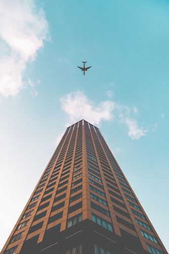 bottom view shot of airplane flying above high rise building