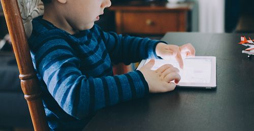 boy sitting on chair beside table using tablet computer