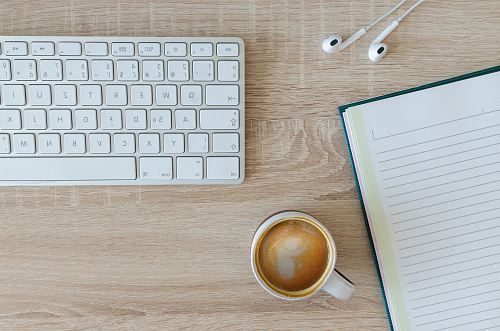 coffee latte near white wireless keyboard and Apple EarPods on the table photography