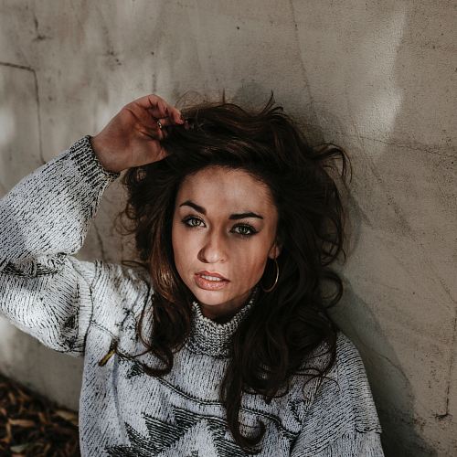 focus photography of woman with left hand on her head while leaning against wall