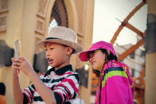 girl watching behind boy holding smartphone