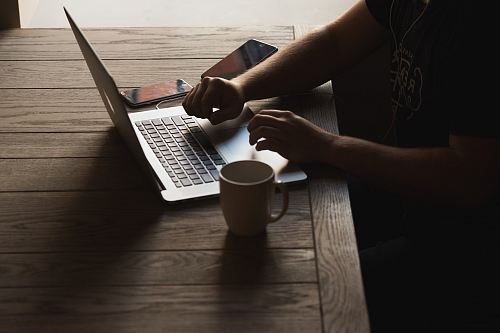 gray laptop computer on brown wooden table beside person sitting on chair