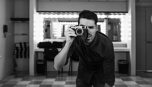 man holding camera bending down in grayscale photography