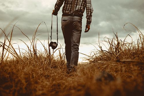 man holding DSLR camera walking through brown grass