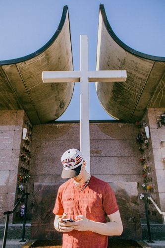 man holding smartphone and standing near cross statue