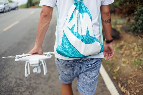 man holding white R/C quadcopter while walking beside concrete roadway